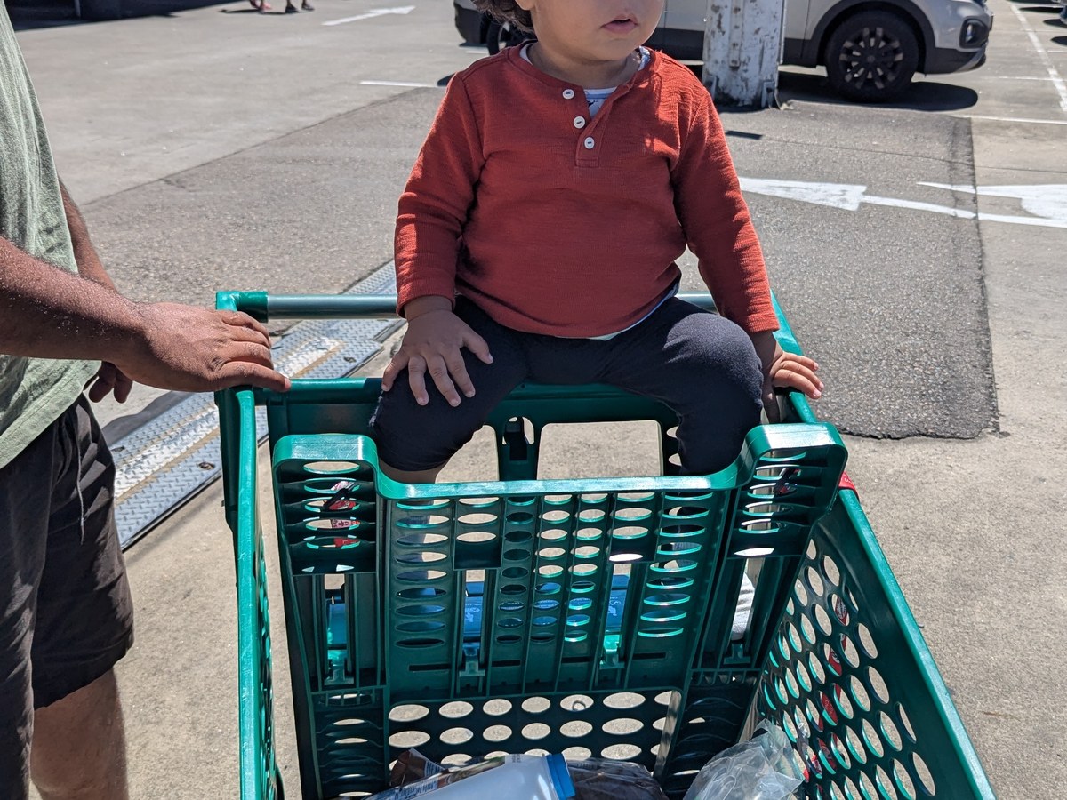 A child in a shopping trolley outside a supermarket